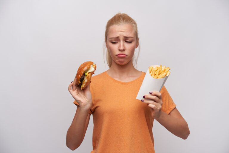 The Worst Fast Food In The World   Upset Young Pretty Blonde Woman Orange T Shirt Keeping Unhealthy Food Her Hands Looking Sadly It Frowning Eyebrows Twisting Her Mouth While Posing White Background 768x512 